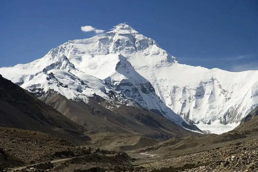 A mountain with snow on it's top and grass below.