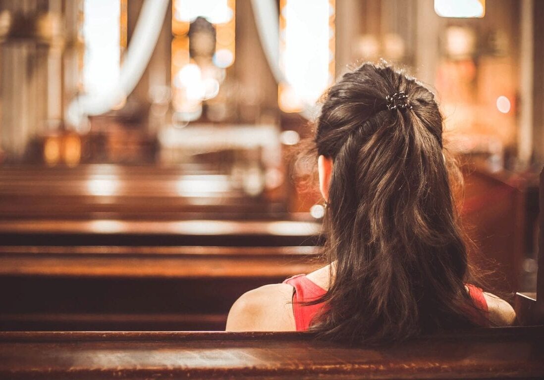 A woman sitting in the middle of a church pews.